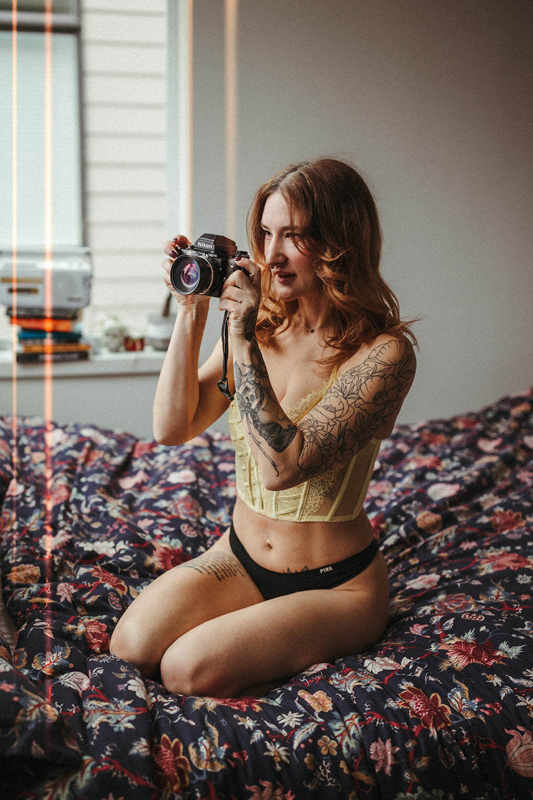 Red haired girl kneels on her bed holding a vintage slr camera
