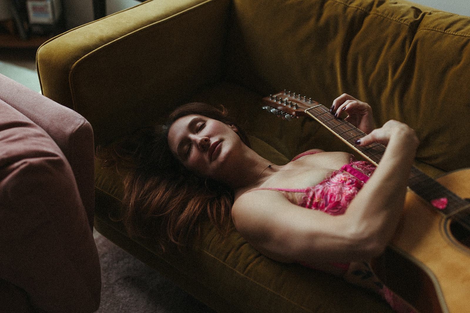 Red haired girl lying on her couch strumming her guitar that rests against her chest